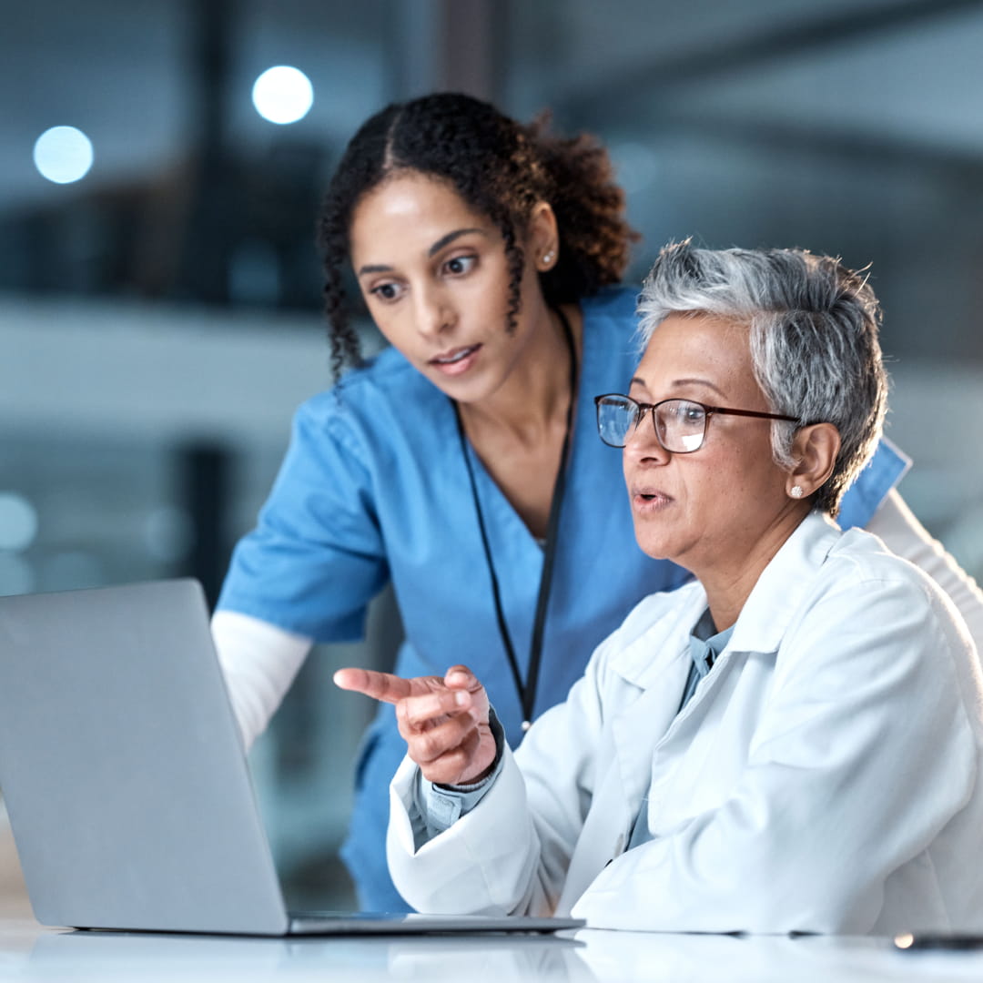 Two healthcare professionals discussing information on a laptop in a modern, well-lit medical office.