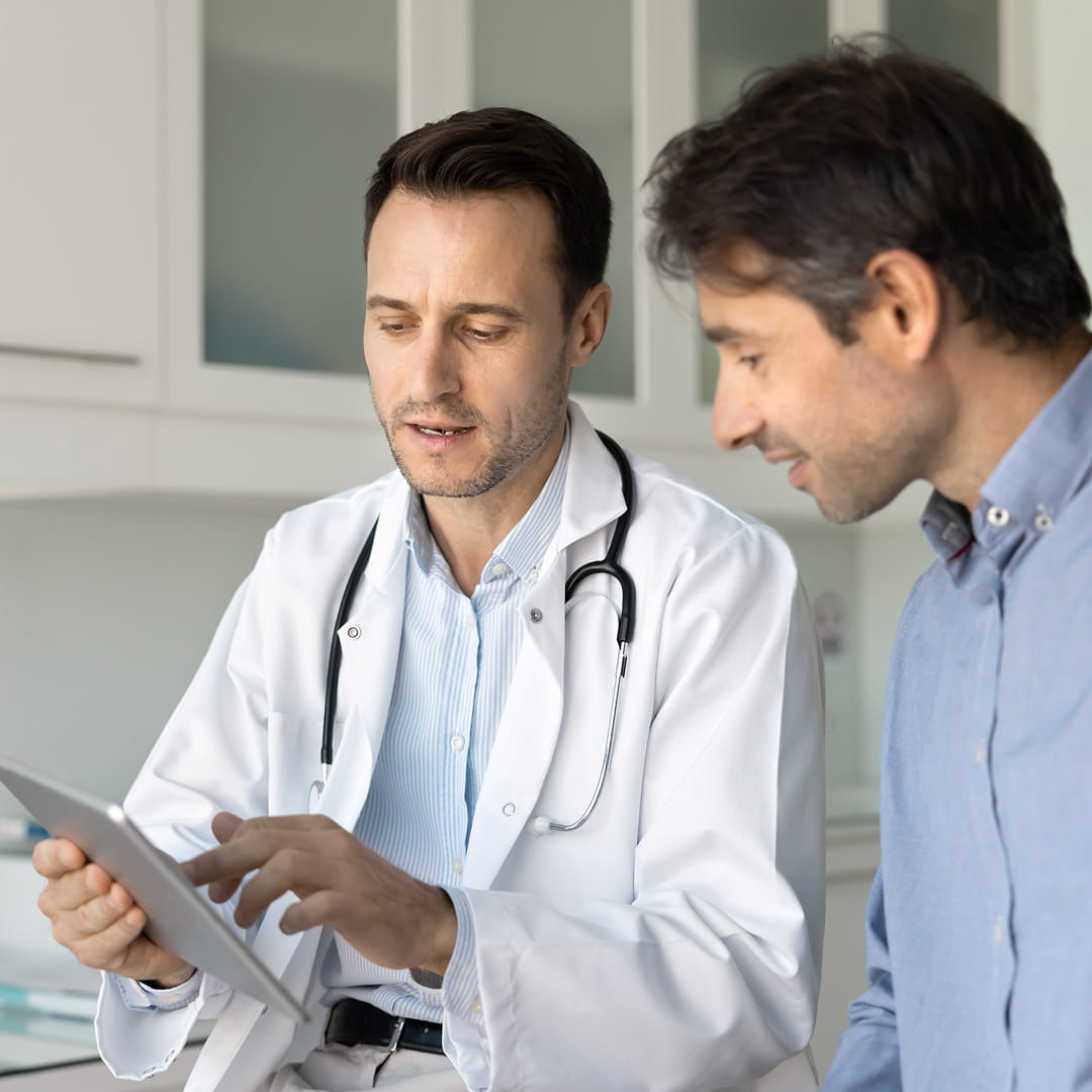 Doctor shows information on a tablet to a man in an office setting. Both are in professional attire.