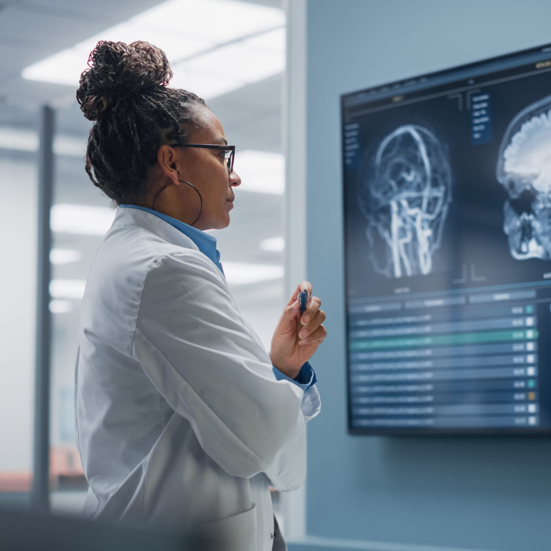 Doctor in a lab coat examines brain scans on a monitor in a medical office.
