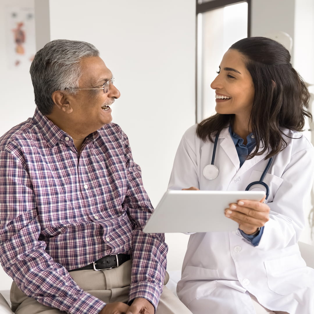 Doctor and elderly man sitting and smiling, discussing a document in a clinic setting.