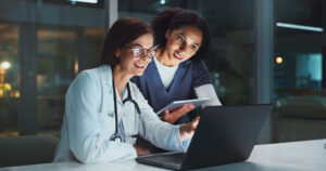 Night, doctor and nurse on laptop for good news or reading online reading schedule in hospital on digital app. Medical results, overtime or happy woman with technology, website info or telehealth.