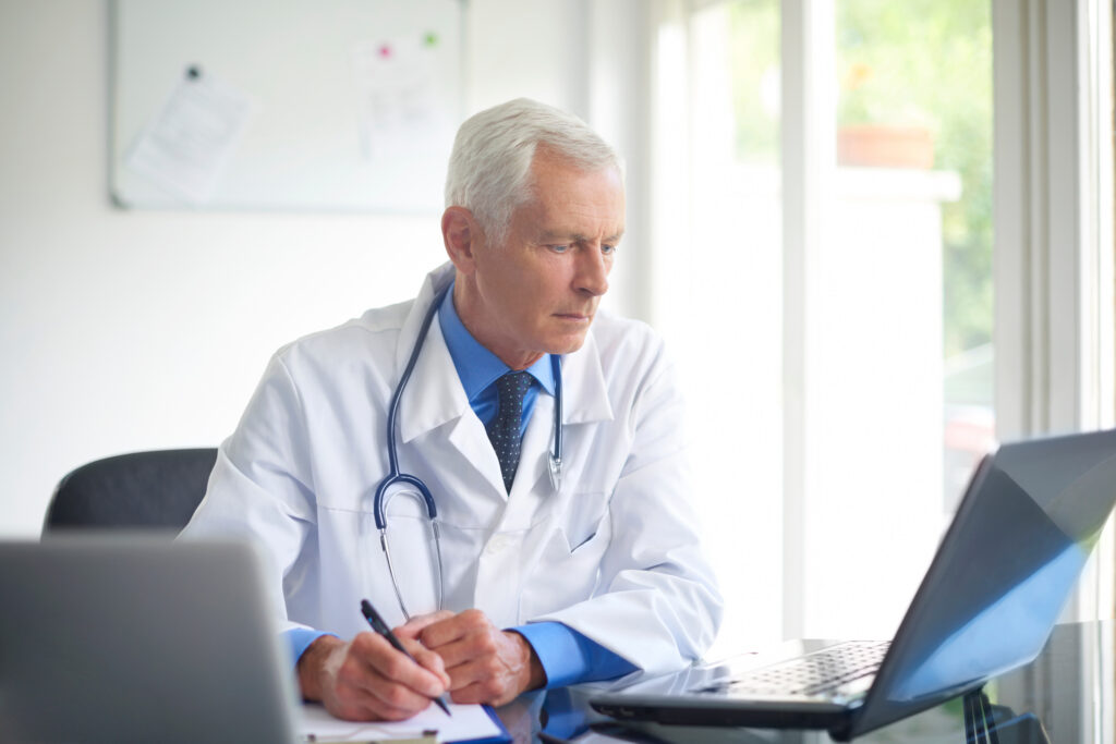 Portrait of male doctor writing down the diagnosis while sitting at consulting room.